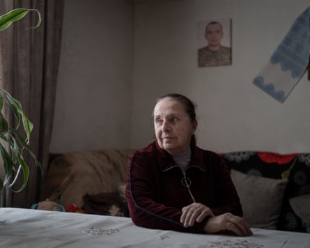 Nataliia Daletska sitting at a dining table with a portrait of her son on the wall behind her