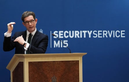 Ken McCallum gives a speech, holding his hands to gesticulate. A sign on the wall behind him reads Security Service, MI5.