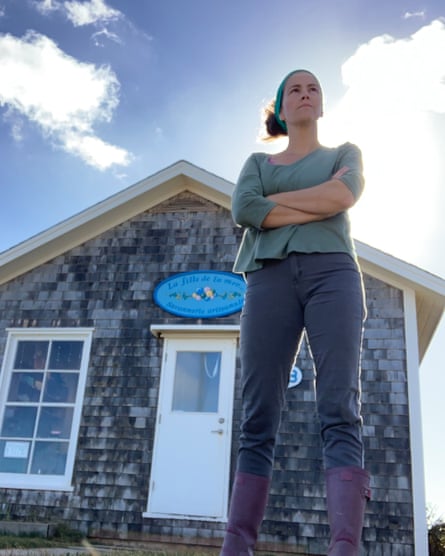 A determined young woman stands with arms folded in front of a wooden house