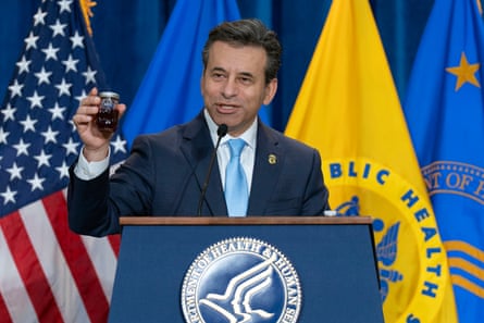 A middle-aged man holds up a jar containing liquid at a lectern with the FDA logo on it.