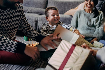 Smiling boy opening Christmas presents with two parents.