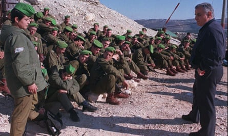 Yitzhak Mordechai stands opposite Israeli soldiers who are mostly seated on a rocky hill. One is standing as they speak to Mordechai
