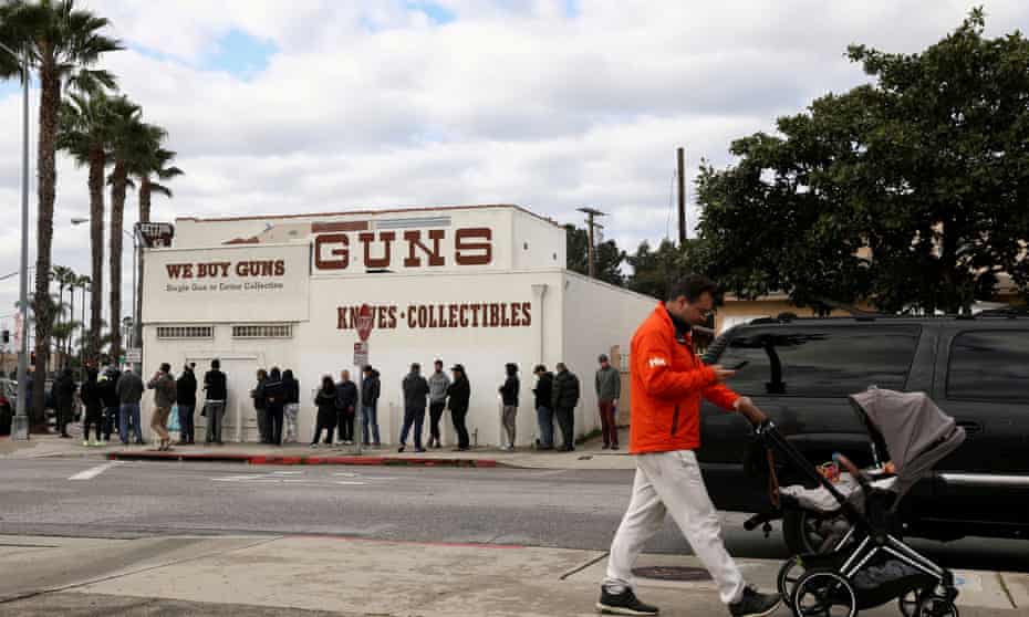 A pedestrian pushes a stroller as people wait in line outside to buy supplies at the Martin B Retting gun store amid fears of the global growth of coronavirus cases, in Culver City, California, on 15 March.