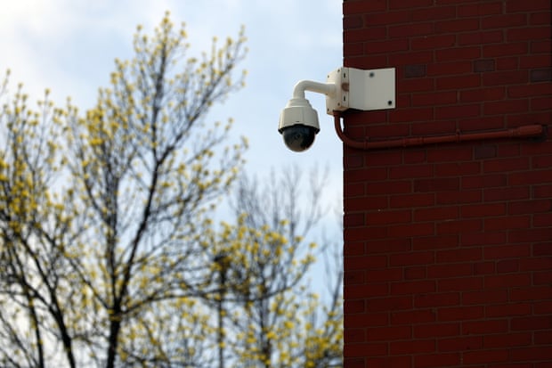 A white dome-shaped camera is mounted to the corner of a red brick building.