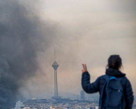 A woman flashes a victory sign while looking over a smoky cityscape