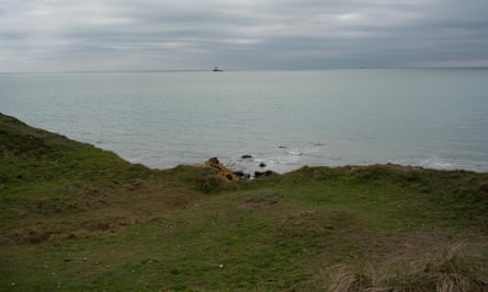 A boat on the horizon of sea and cloudy sky with grassy shore in foreground