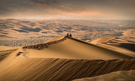 A couple sitting on the top of a giant sand dune in the desert watching the sunset in the Empty Quarter, or Rub al Khali, the world’s largest sand desert