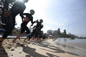 Triathlon competitors in swimming costumes race toward the water