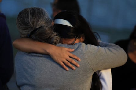 With faces obscured, what appears to be a younger women or girl, with a white headband in her hair, hugs an older woman with graying hair.
