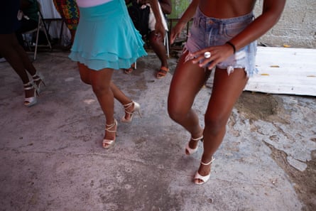 Two black women wearing heeled dance shoes, one in denim shorts, one in a short blue skirt, rehearse dance steps