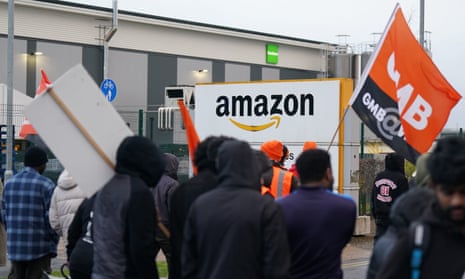 Amazon warehouse with people in jackets in front with their backs to camera and one waving a GMB orange and black flag