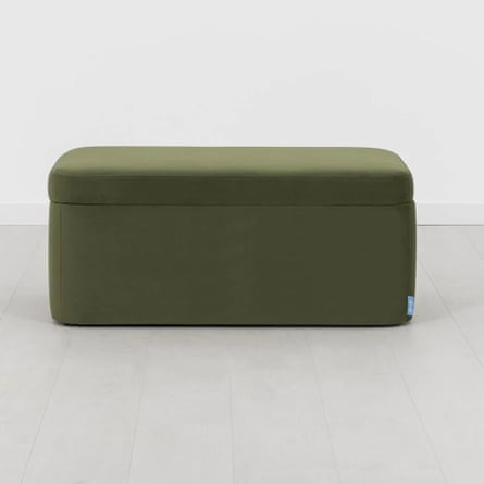 A green storage ottoman on a grey floor and background