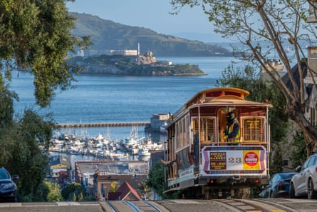 A street car cresting a hill over San Franciso, looking down to the water of the bay.