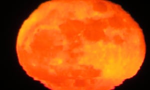 A hazy orange moon seen through the atmosphere.
