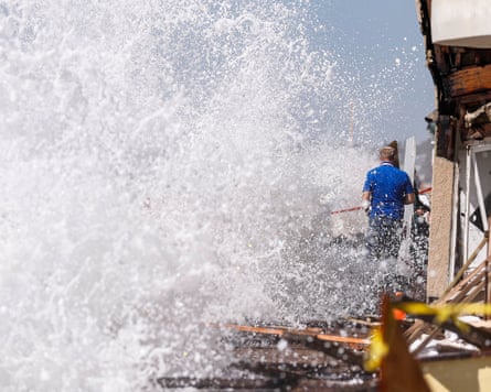Residents stand on the pier after waves crash along the Peninsula in Long Beach, California.
