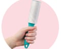 A hand holds a lint roller against a pink background