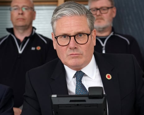 Keir Starmer, dressed in a black suit, sitting in front of a dark phone with a serious expression on his face.