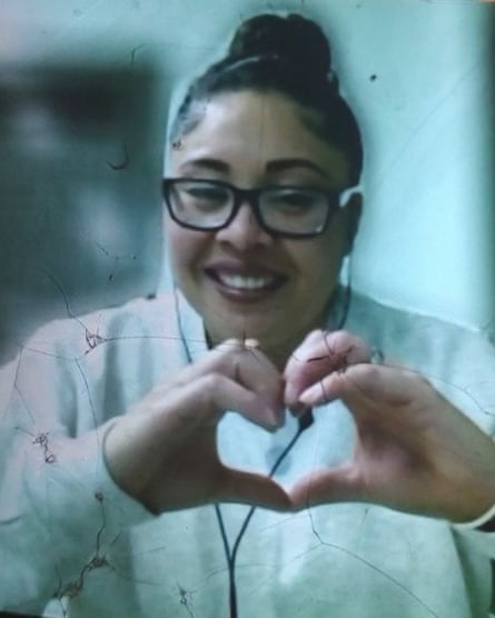 A person with glasses and hair in a bun smiling and making a heart shape with their hands.