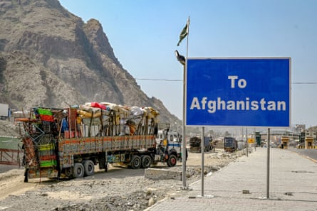 A queue of huge trucks laden with mattresses, beds and other household goods beside a large blue sign saying ‘To Afghanistan’