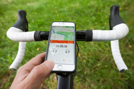 Closeup of a smartphone mounted on to the handlebars of a road bike in a park. The phone is displaying the Strava app