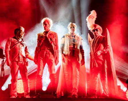 The four members of Duran Duran in white Halloween costumes on stage backlit in red.