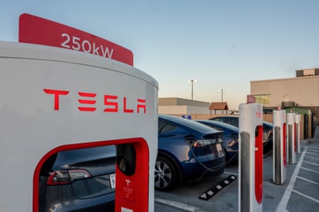 Tesla electric vehicles charging at red and white Supercharger stations in a parking lot