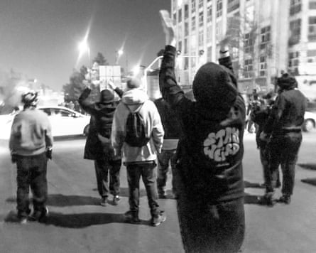People protesting after dark, seen from behind, in a grainy black and white image from the streets of Tehran.