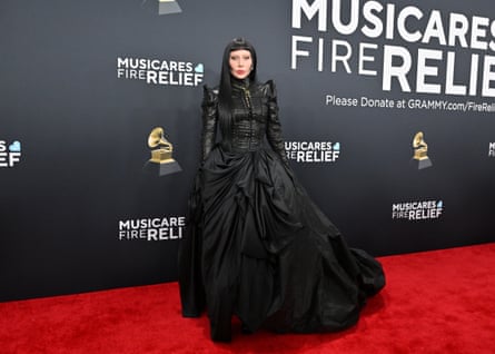 CDATA[## The Stage as a Dress: Samuel Lewis's Vision for Lady Gaga
It begins in a cascade of crimson: a stage draped in red curtains, lights flashing in scarlet hues. This is **Lady Gaga**, where theatricality is expected. As the lights brighten, it becomes clear she isn't standing on a massive stage—she's wearing it.
A militaristic bodice extends into the sweeping velvet drapes of a **7.5-meter-high gown**. "It's not just a dress; it's a moving piece of art, an **engineering feat**," explains Australian-Taiwanese designer Samuel Lewis, who conceived the design in collaboration with LA-based costume designer Athena Lawton.
The full scope of the costume reveals itself when Gaga's skirt opens to expose a metal cage beneath, with dancers twisting and reaching behind its steel bars. Lewis pushed his creative boundaries to envision and execute this design. "We had to ask, how enormous can something like this be?"
![Lady Gaga in a black goth gown with a black wig on a red carpet