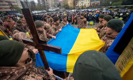 A guard covers a coffin with the Ukrainian flag during the burial ceremony at the Lychakiv cemetery