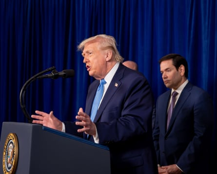 Donald Trump gestures as he speaks into a microphone at a lectern, with Marco Rubio standing in the background