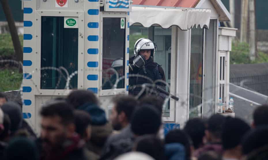 A Greek border guard observes people on the Turkish side of a border crossing