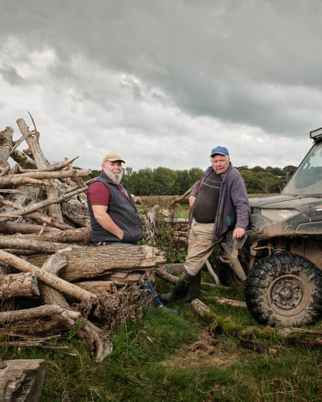 Farmers Derek Gow and Derek Banbury, one leaning against logs, the other a farm vehicle