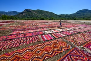 A child runs between colourful carpets laid out in open fields overlooked by mountains in the distance under a blue sky