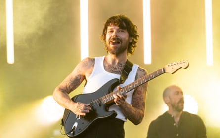 Simon Neil plays guitar in front of yellow lights