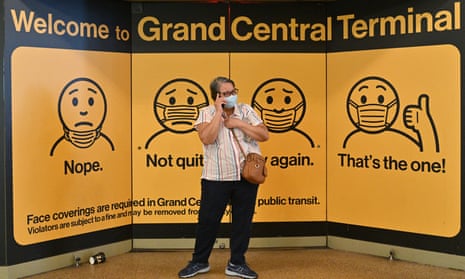 A person wearing a face mask stands in front of a sign explaining how to wear one properly in Grand Central Terminal in New York City. 