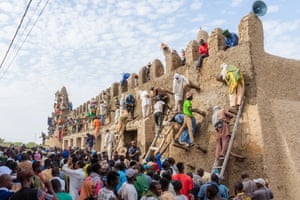 A crowd watches people standing on ladders, applying plaster to the outer walls of the mosque.