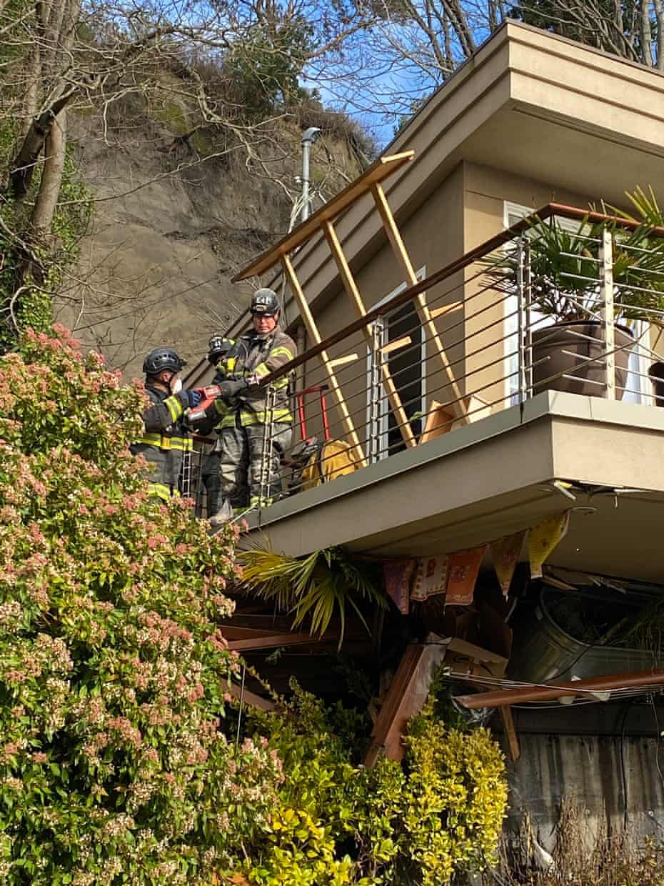 Three firefighters stand on the deck of a home whose foundation has collapsed