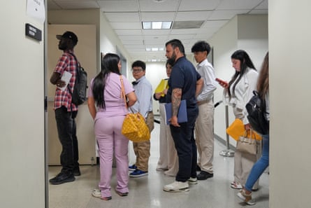 People standing in a line in a hallway lit by overhead fluorescent light.