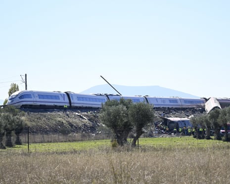 A derailed train carriage lies overturned near AVE train cars as rescue workers gather below