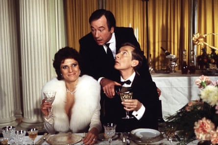 Butler Jack Douglas pours a drink for Kenneth Williams, wearing a dinner suit, and ogles Suzanne Danielle, in a fur coat