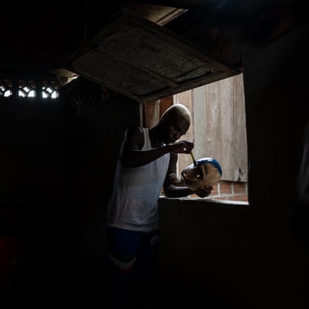 A man stands by an open window painting a wooden mask in blue paint