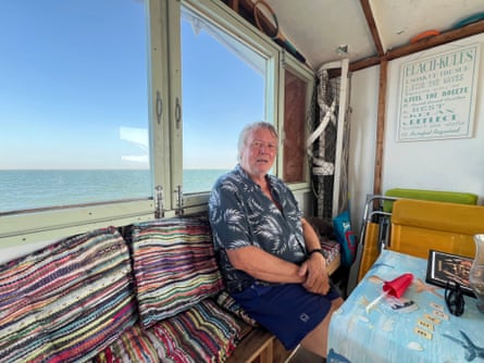 Giles Watling sitting on a colourful stripey bench in a beach hut