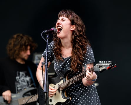 Karly Hartzman wears a spotted dress while holding a guitar and singing on stage at the Green Man festival.