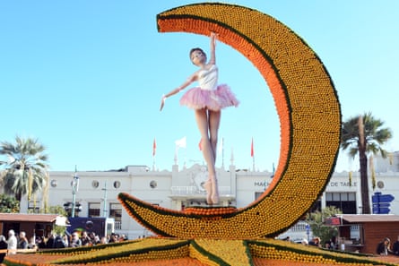 A large crescent moon covered with lemons and oranges with a model of a ballerina in a tutu standing inside it