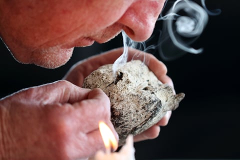 Man's face leaning over a piece of white ambergris with thin tendril of smoke rising from it