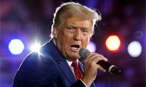 Trump speaks into microphone with spotlights shining in the background