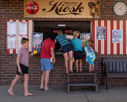 Six children in T-shirts and shorts stand at a kiosk. Four of them are on a stepladder
