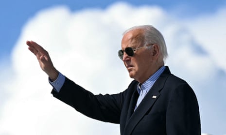 An older white man in a suit wearing aviators waves from what appears to be the top of an airplane stairway on tarmac.