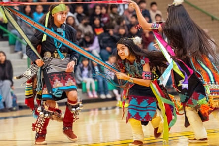 Performers in traditional dress holding ribbons, in a sports hall
