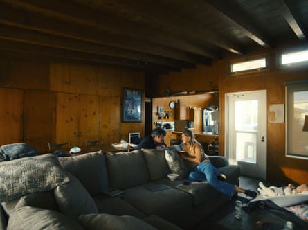 Nathan Fielder and Elizabeth Holmes lean close on a couch in a wood-panelled living room, a baby nearby